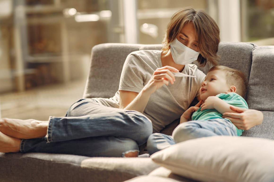 A caring mother checks her son's temperature while they relax on a sofa, showcasing parent-child affection and health care.