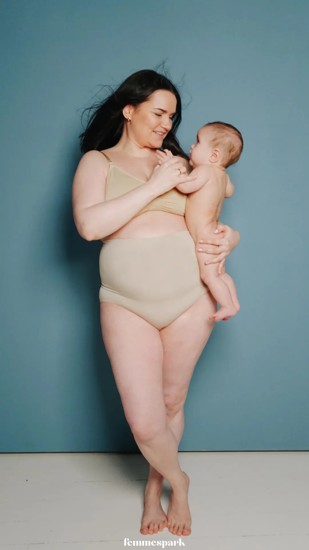 A woman in underwear holding her baby, showcasing her postpartum body with a gentle smile, highlighting body changes after birth and the beauty of the postpartum figure.
